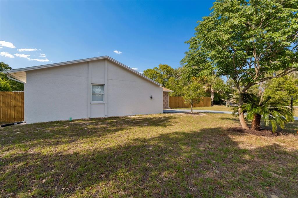 A side view of a light-colored house with a single window and a grassy yard — 9015 FOREST OAKS BOULEVARD, SPRING HILL, FL