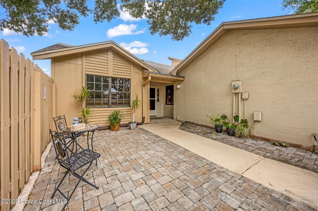 A paved courtyard features a small bistro set, potted plants, and a tan exterior wall — 1311 ISLAND GREEN DRIVE NE UNIT B2-12, PALM BAY, FL