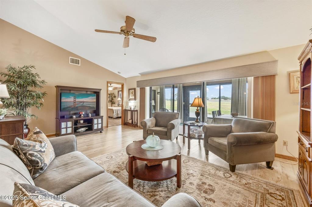 A living room features a vaulted ceiling, wood-look flooring, two armchairs, and a sliding glass door — 1311 ISLAND GREEN DRIVE NE UNIT B2-12, PALM BAY, FL
