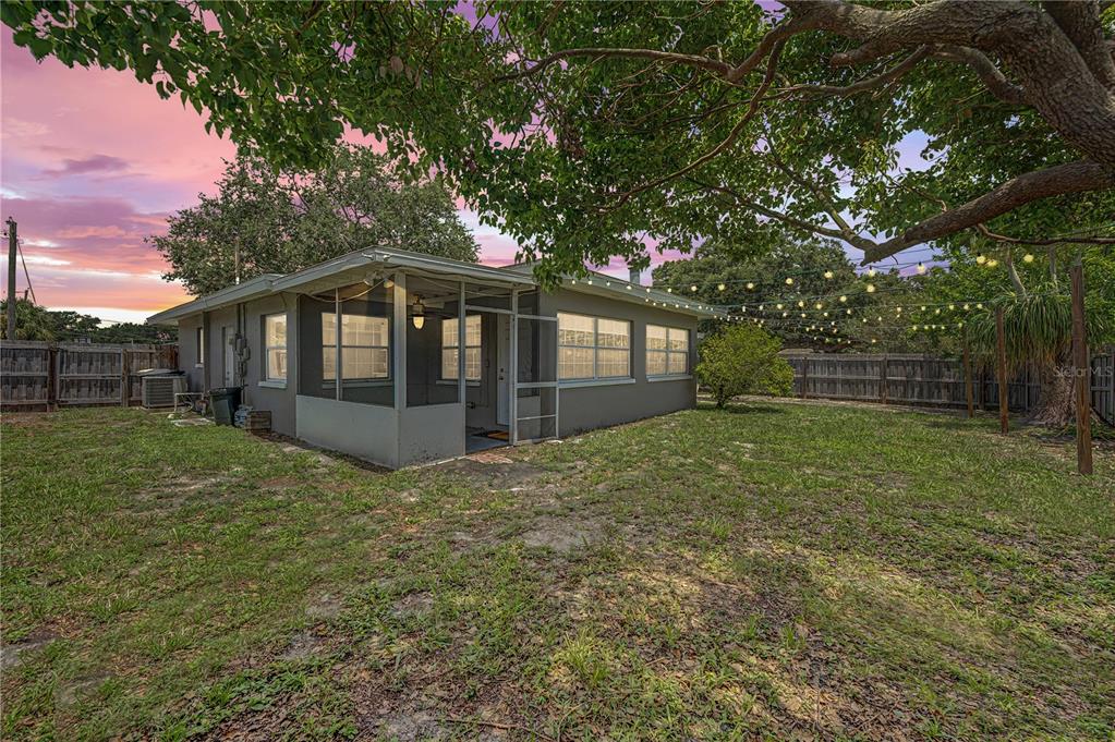 A gray house with a screened-in porch stands in a grassy backyard under a sunset sky — 1223 S SAN REMO AVENUE, CLEARWATER, FL