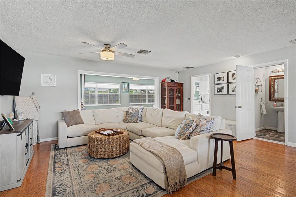 A living room features a large sectional sofa, a woven ottoman, and hardwood flooring — 1223 S SAN REMO AVENUE, CLEARWATER, FL
