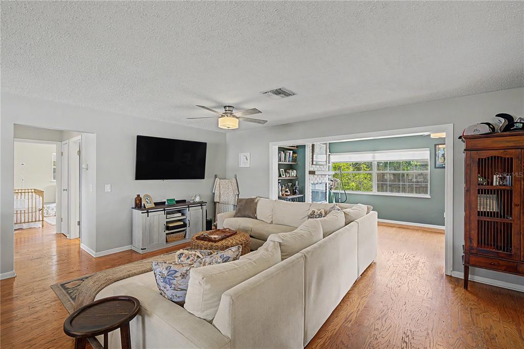 A living room features a sectional sofa, a wall-mounted television, and hardwood flooring — 1223 S SAN REMO AVENUE, CLEARWATER, FL