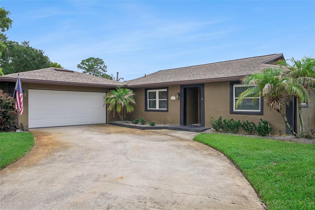 A brown single-story house features a white garage door, a concrete driveway, and palm trees — 636 SWALLOW DRIVE, CASSELBERRY, FL