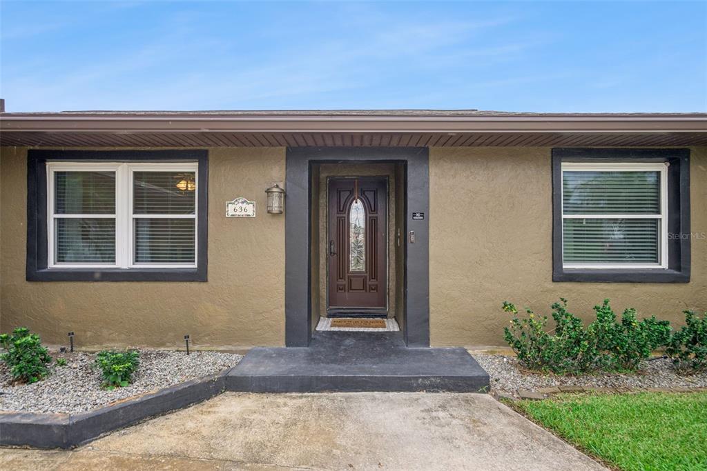 The exterior of a single-story house features a brown stucco facade, a dark front door, and two windows — 636 SWALLOW DRIVE, CASSELBERRY, FL