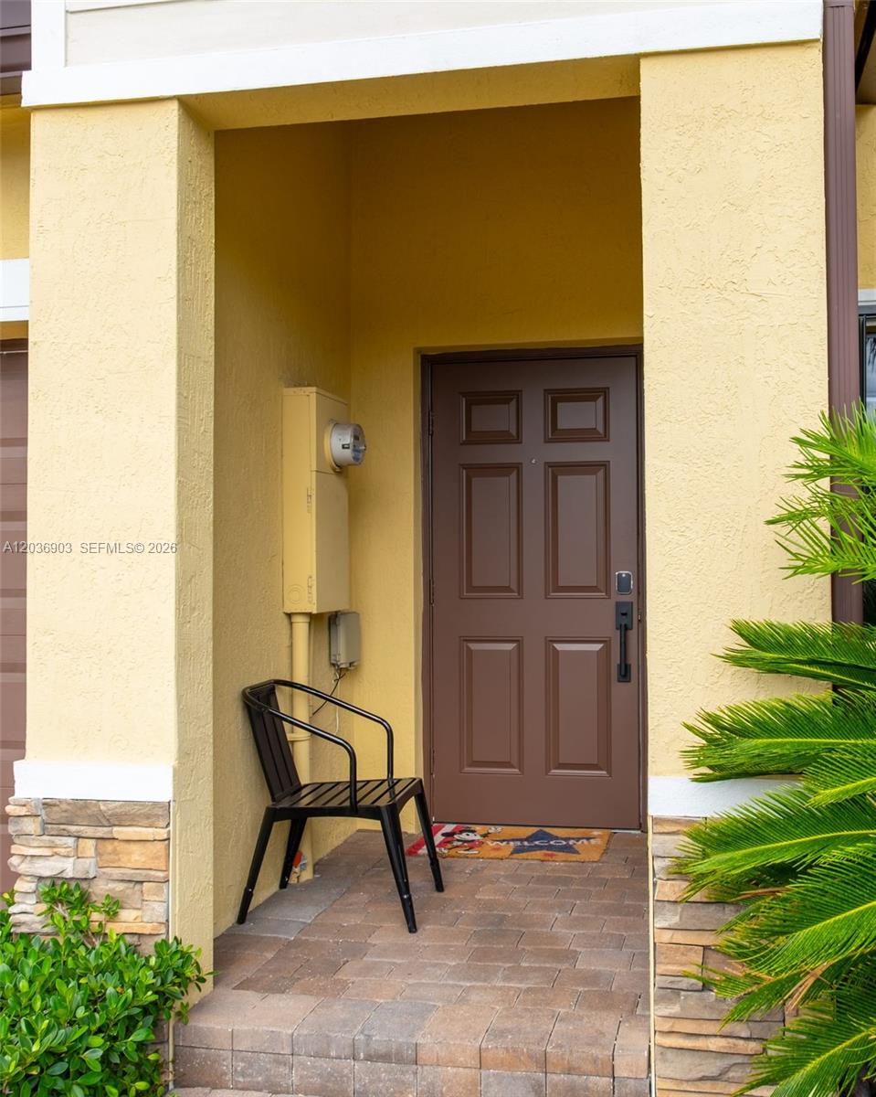 A brown front door is set in a yellow stucco entryway with a black chair — 4715 Caspian Way, Davie FL 33314, DAVIE, FL