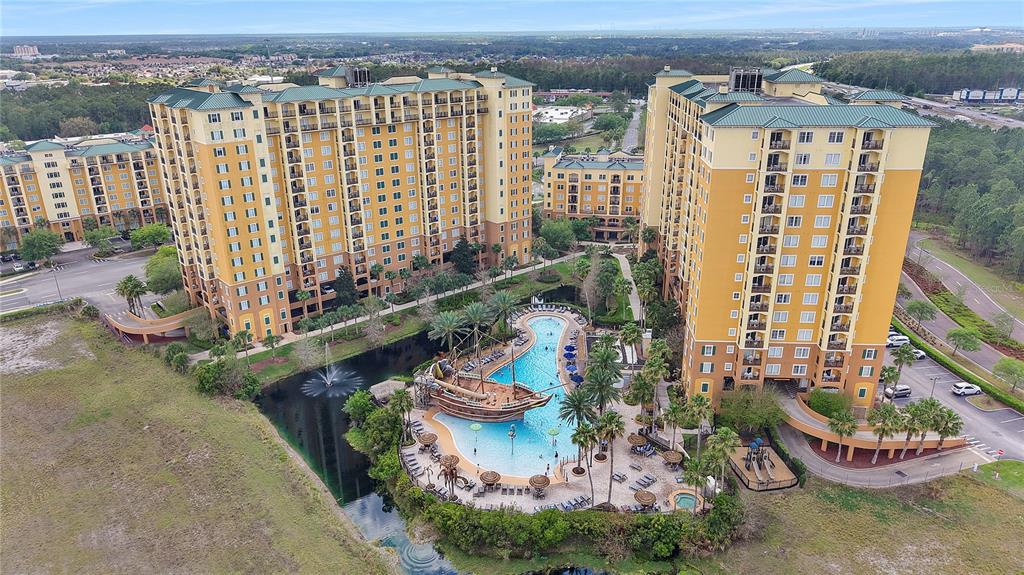 An aerial view shows two tall yellow apartment buildings surrounding a pool with a pirate ship — 8112 POINCIANA BOULEVARD UNIT 1306, ORLANDO, FL