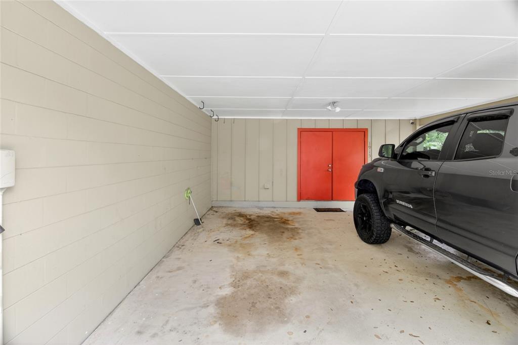 A covered carport with a concrete floor, beige block walls, and bright orange double doors — 1915 NW 42ND PLACE, GAINESVILLE, FL