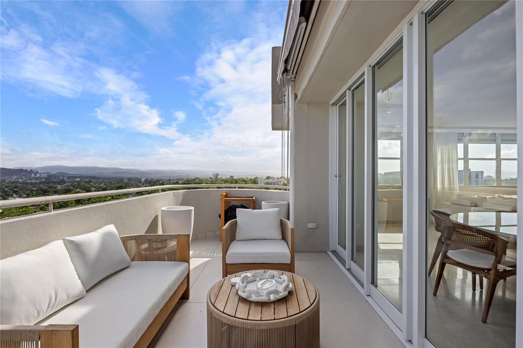 A balcony with outdoor seating overlooks a distant landscape under a blue sky — 225 ROAD NO 2, VILLA CAPARRA PLAZA UNIT PH-3, GUAYNABO, PR