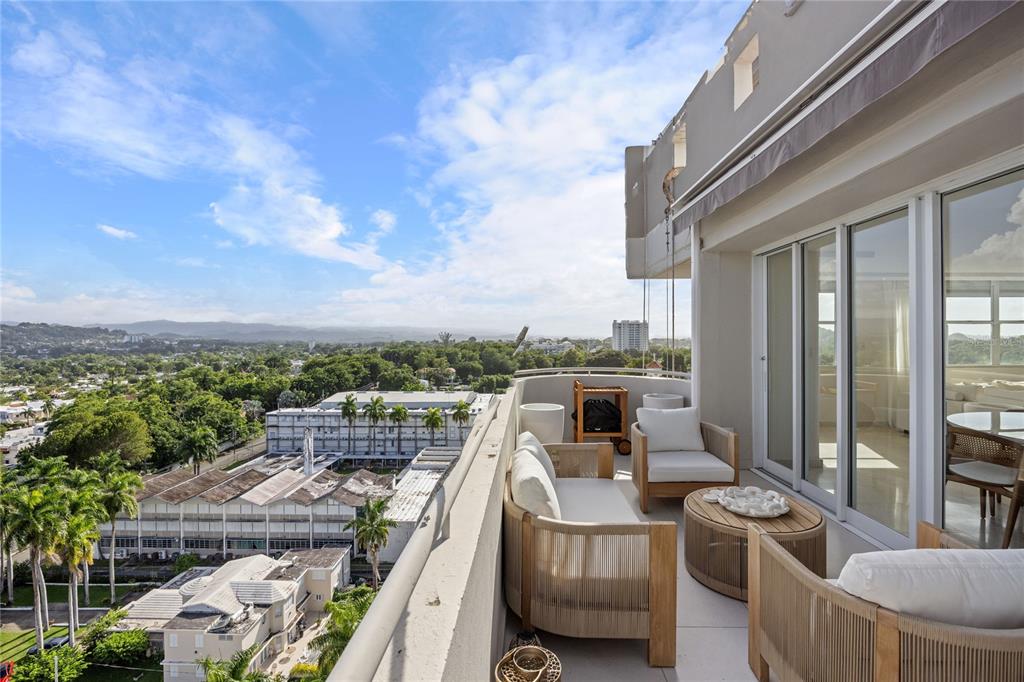 A high-rise balcony features outdoor furniture overlooking a suburban landscape with trees and buildings — 225 ROAD NO 2, VILLA CAPARRA PLAZA UNIT PH-3, GUAYNABO, PR
