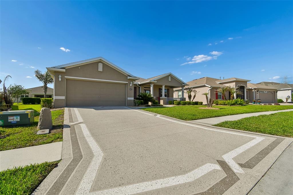 A tan single-story house with a two-car garage and a decorative concrete driveway — 26617 OTTER CREEK LANE, LEESBURG, FL