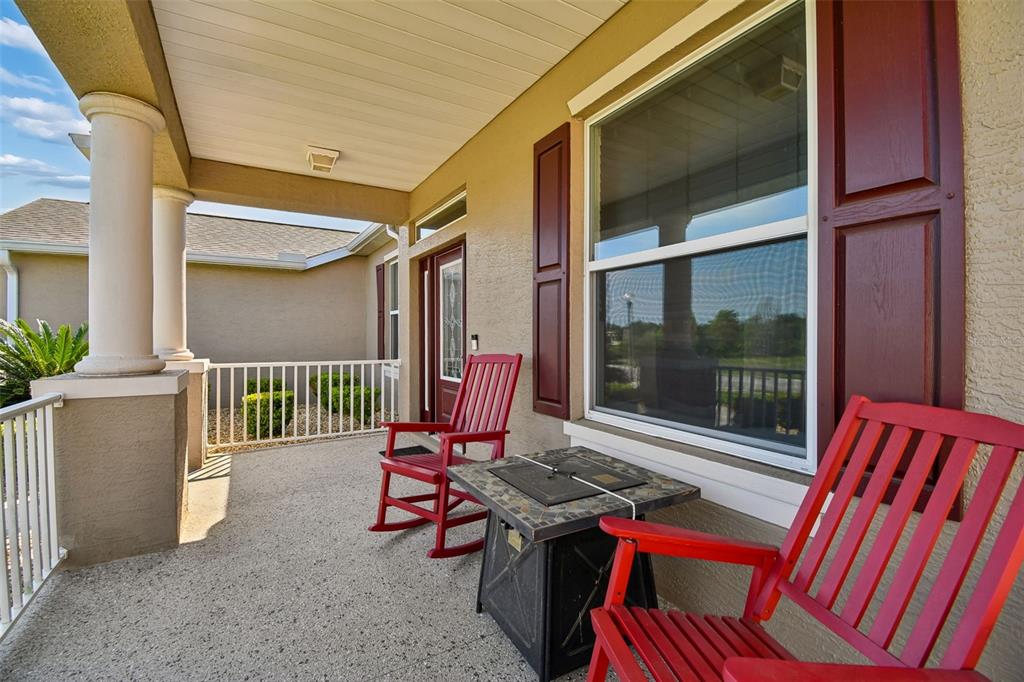 A covered front porch features two red rocking chairs and a small fire pit table — 26617 OTTER CREEK LANE, LEESBURG, FL