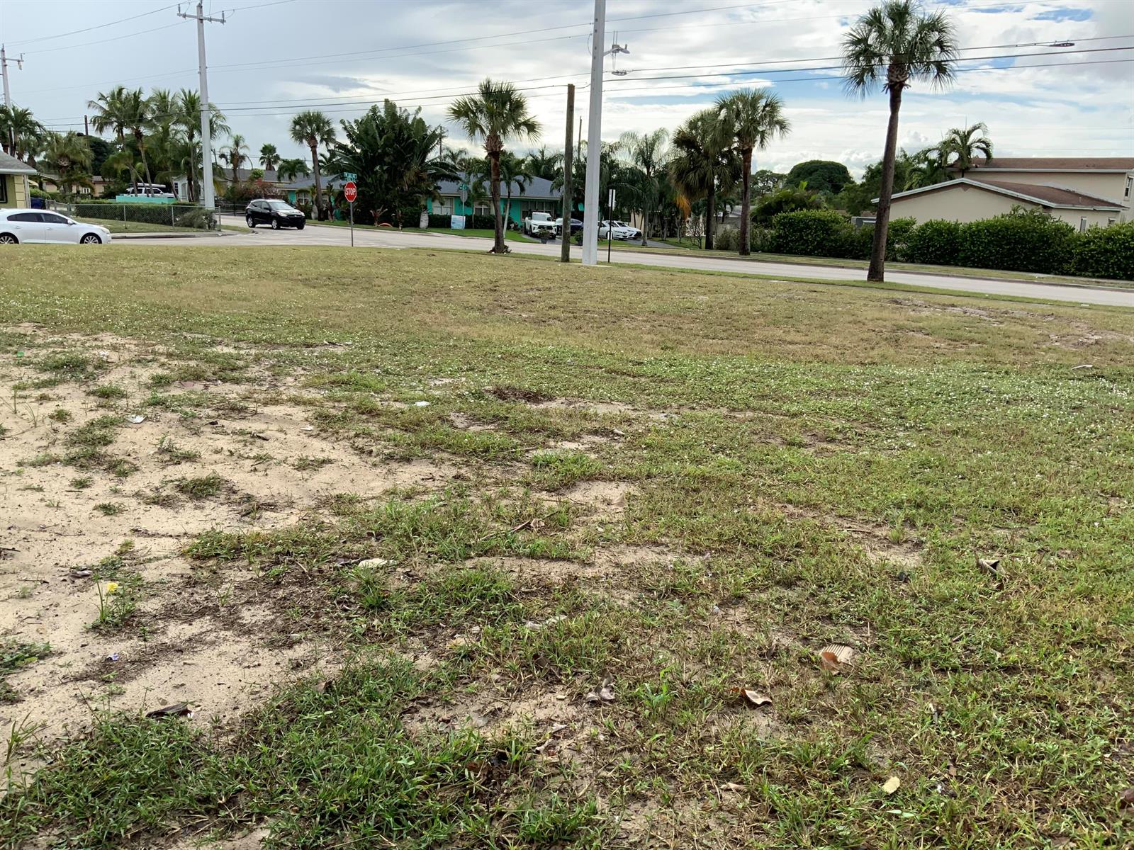A vacant, grassy lot with sandy patches sits alongside a paved road with palm trees — Null 32nd & S Ave S, Riviera Beach FL 33404, RIVIERA BEACH, FL