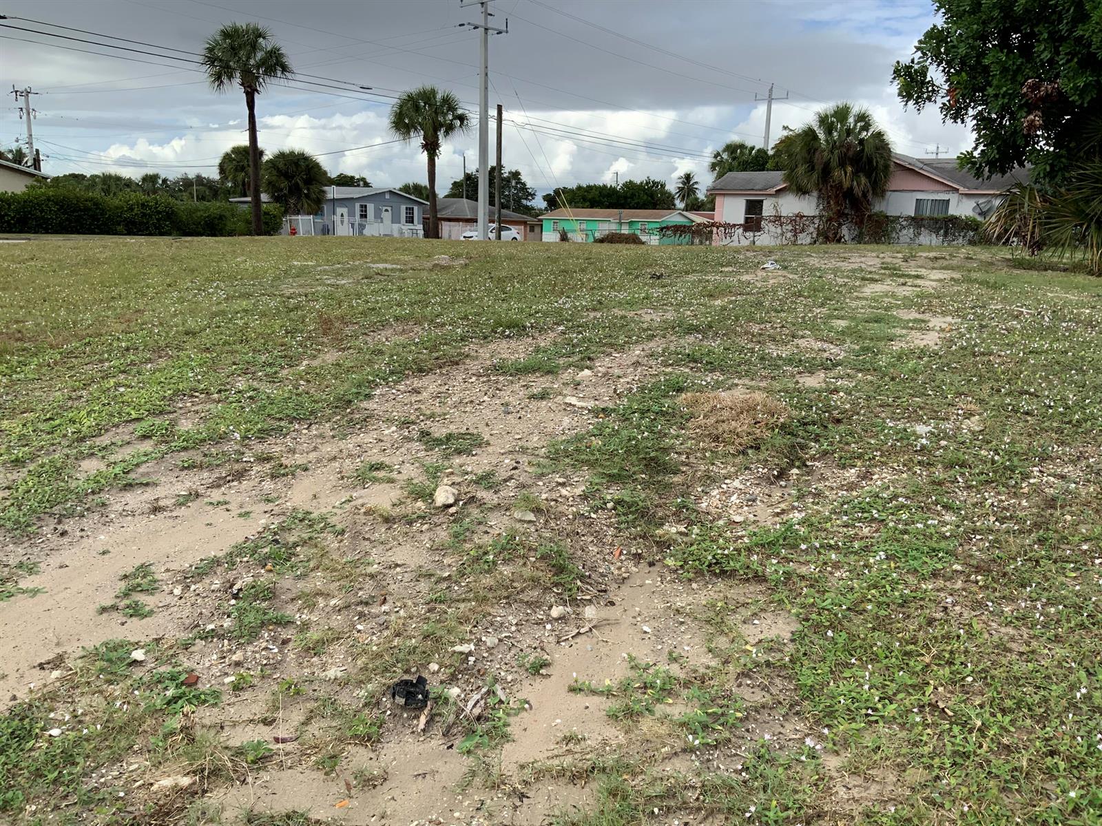 An empty, grassy residential lot with scattered rocks and palm trees in the background — Null 32nd & S Ave S, Riviera Beach FL 33404, RIVIERA BEACH, FL