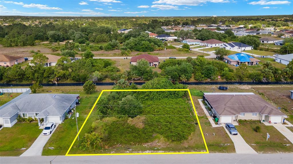 An aerial view shows a vacant, overgrown residential lot outlined in yellow between two houses — 1518 HAVILAND AVE S, LEHIGH ACRES, FL