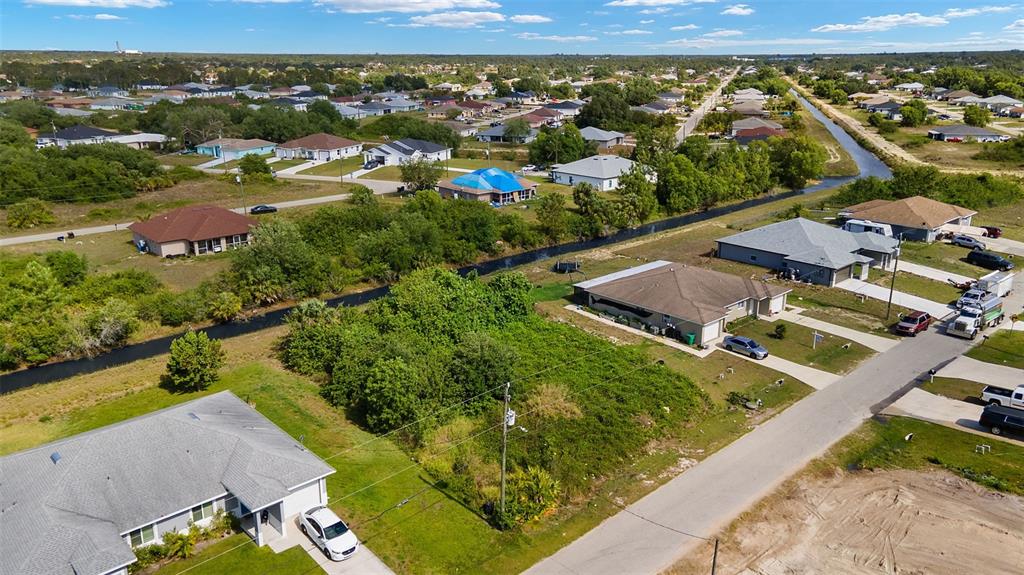An aerial view shows a vacant residential lot situated between two houses near a canal — 1518 HAVILAND AVE S, LEHIGH ACRES, FL