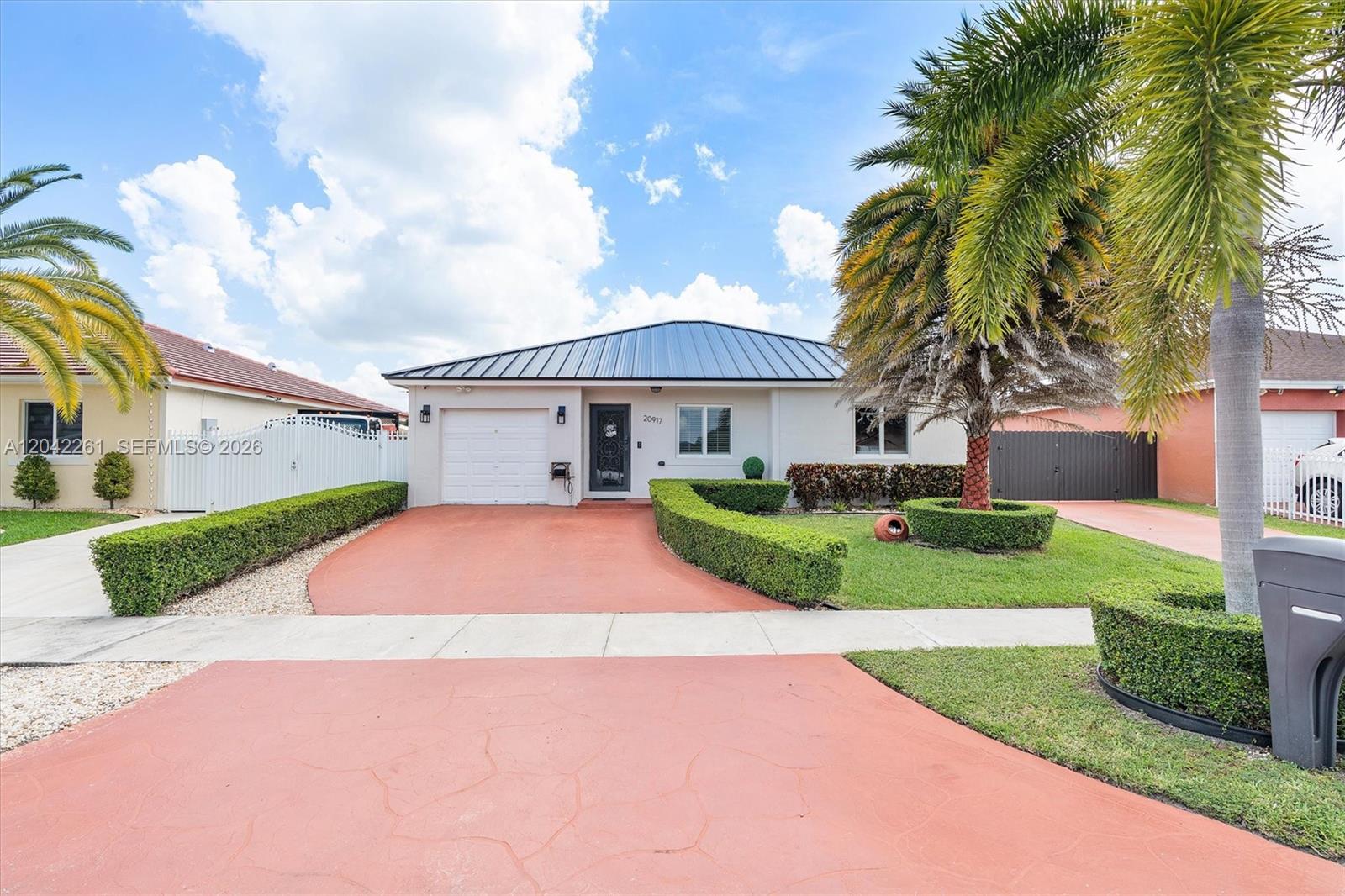 A single-story house with a metal roof, a red driveway, and manicured hedges — 20917 SW 125th Ave Rd, Miami FL 33177, MIAMI, FL