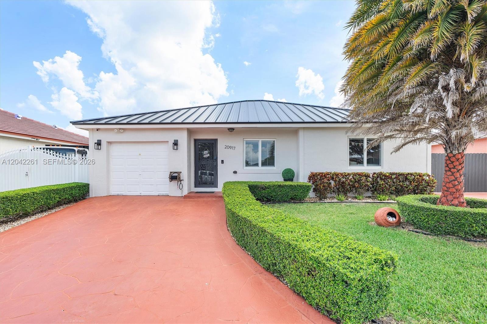 A single-story house with a metal roof, a red driveway, and a manicured hedge — 20917 SW 125th Ave Rd, Miami FL 33177, MIAMI, FL