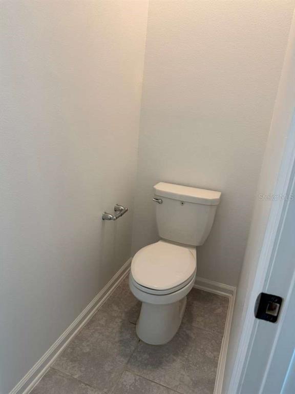 A small bathroom features a white toilet, light gray walls, and gray tile flooring — 2312 BROOK MARSH LOOP, KISSIMMEE, FL