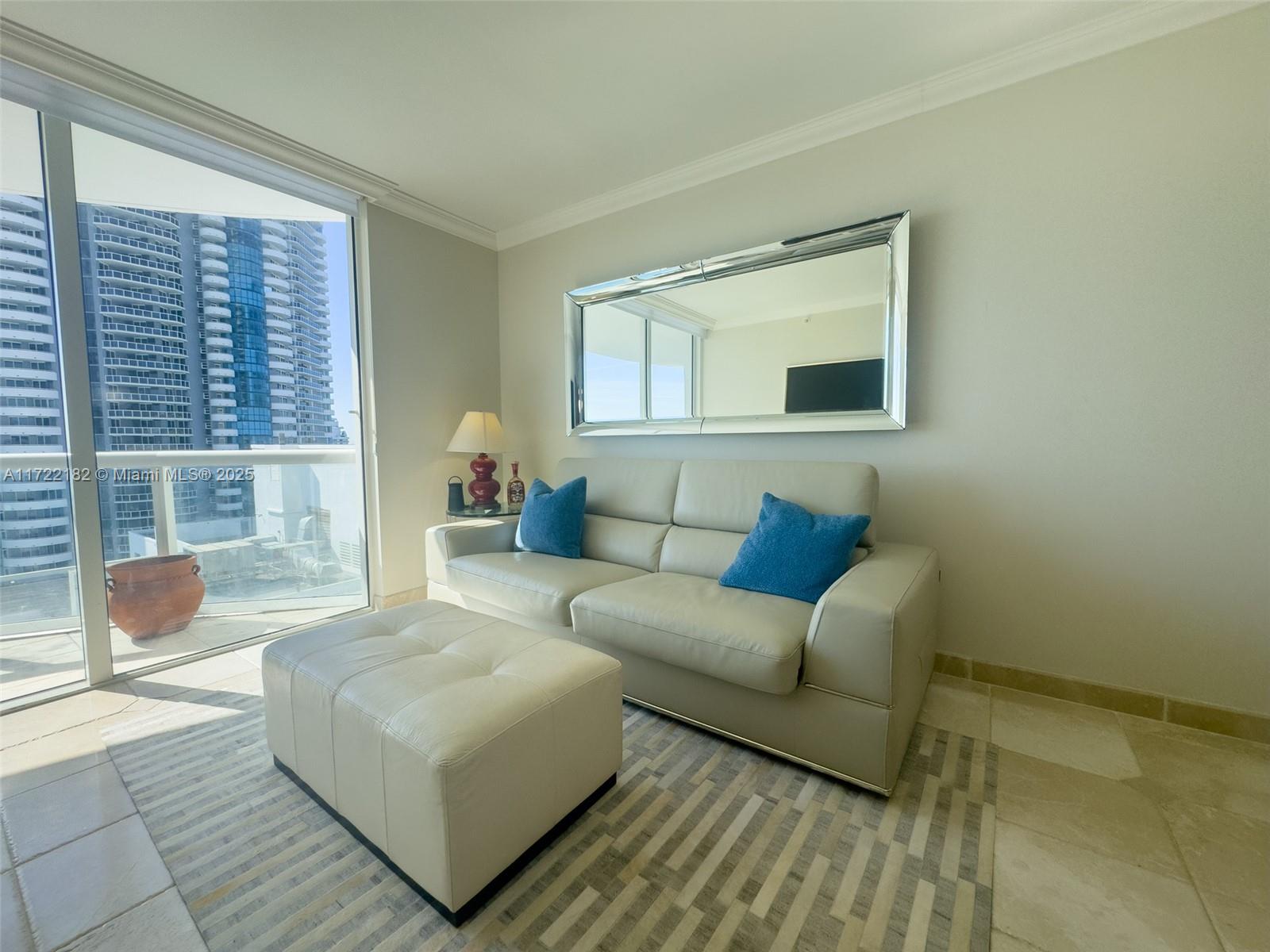A living room features a light-colored sofa, matching ottoman, large wall mirror, and balcony view — 6365 Collins Ave # 1506, Miami Beach FL 33141, MIAMI BEACH, FL