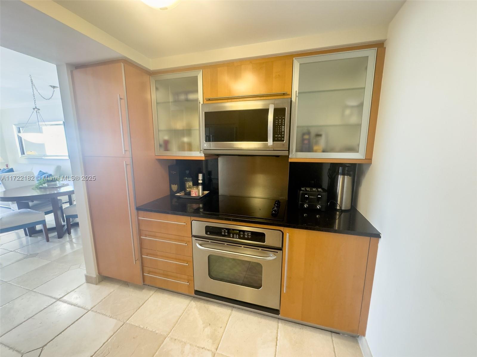 A kitchen features light wood cabinets, stainless steel appliances, and black countertops — 6365 Collins Ave # 1506, Miami Beach FL 33141, MIAMI BEACH, FL