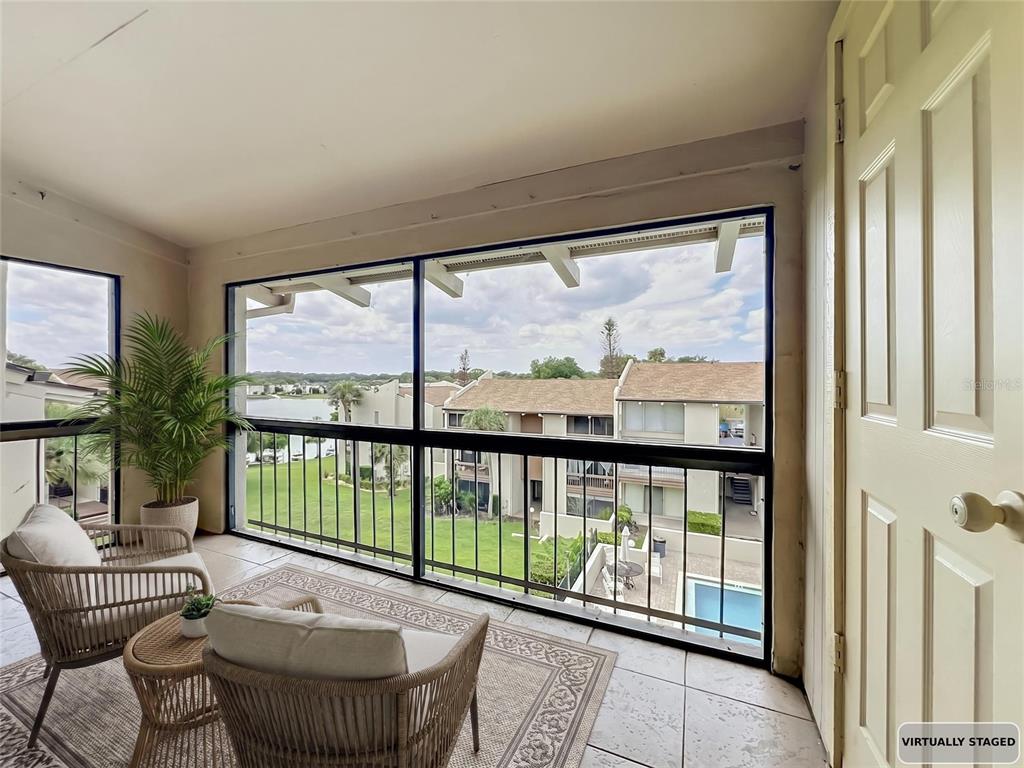 A screened-in balcony with tile flooring overlooks a residential complex, a pool, and a lake — 568 ORANGE DRIVE UNIT 50, ALTAMONTE SPRINGS, FL