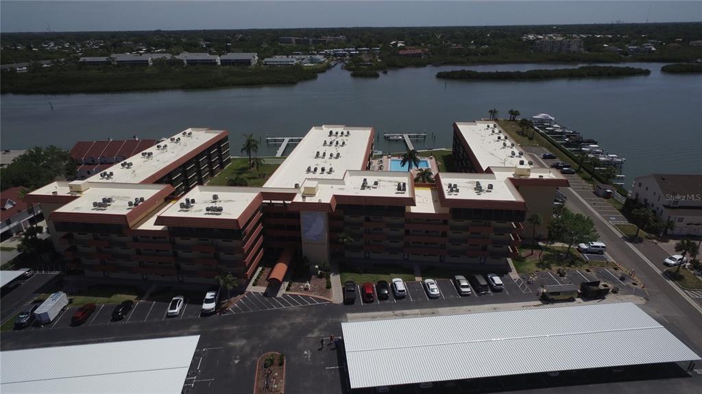 An aerial view shows a multi-story apartment complex with a parking lot and boat docks — 19701 GULF BOULEVARD UNIT 212, INDIAN SHORES, FL