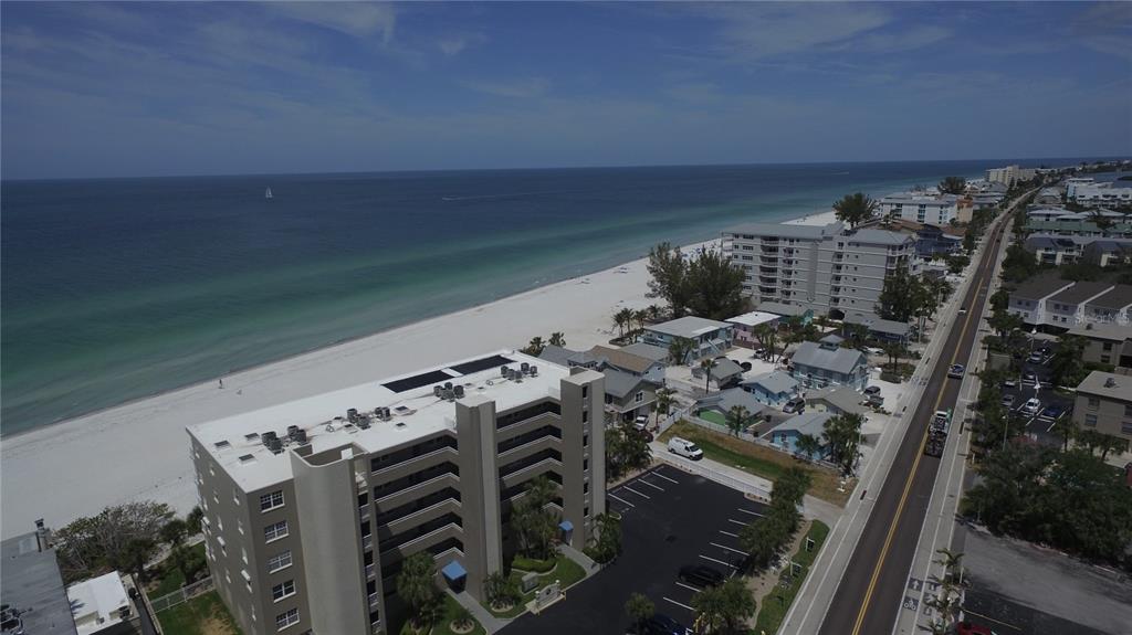 An aerial view shows a beach with white sand, turquoise water, and nearby buildings — 19701 GULF BOULEVARD UNIT 212, INDIAN SHORES, FL