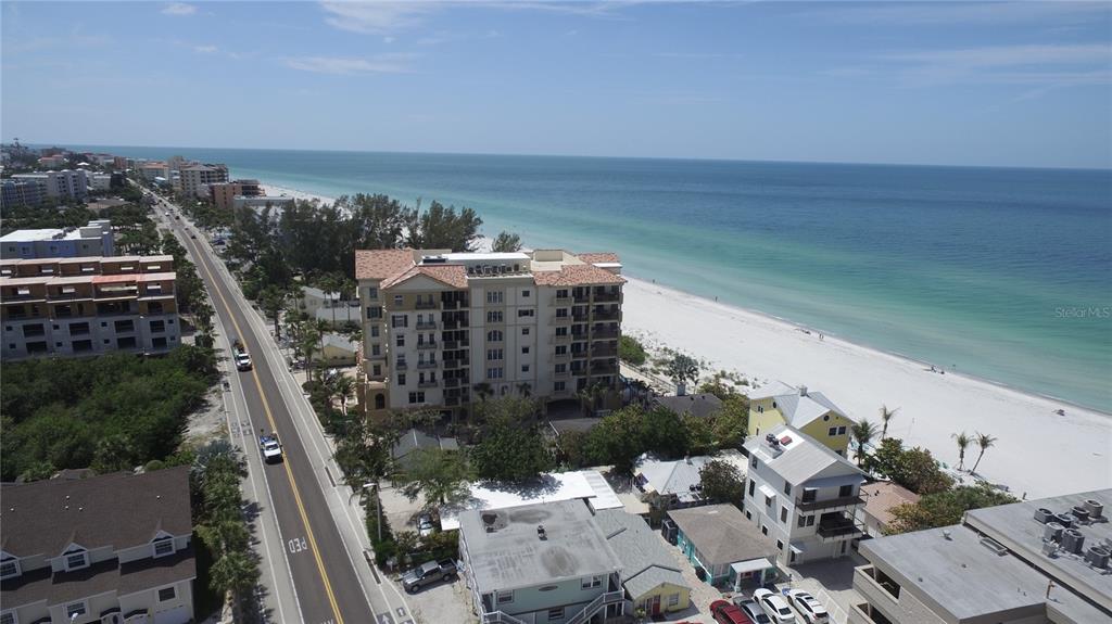 An aerial view shows a multi-story beachfront condominium building next to a coastal road — 19701 GULF BOULEVARD UNIT 212, INDIAN SHORES, FL