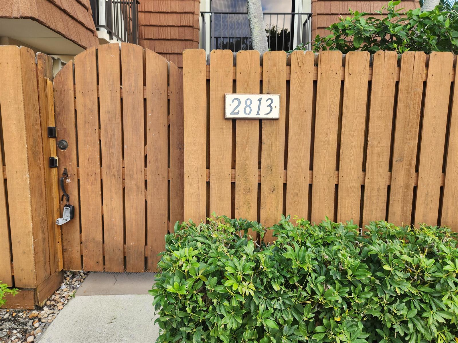 A wooden fence with a gated entrance and a house number sign sits behind bushes — 2813 28th Court, Jupiter FL 33477, JUPITER, FL