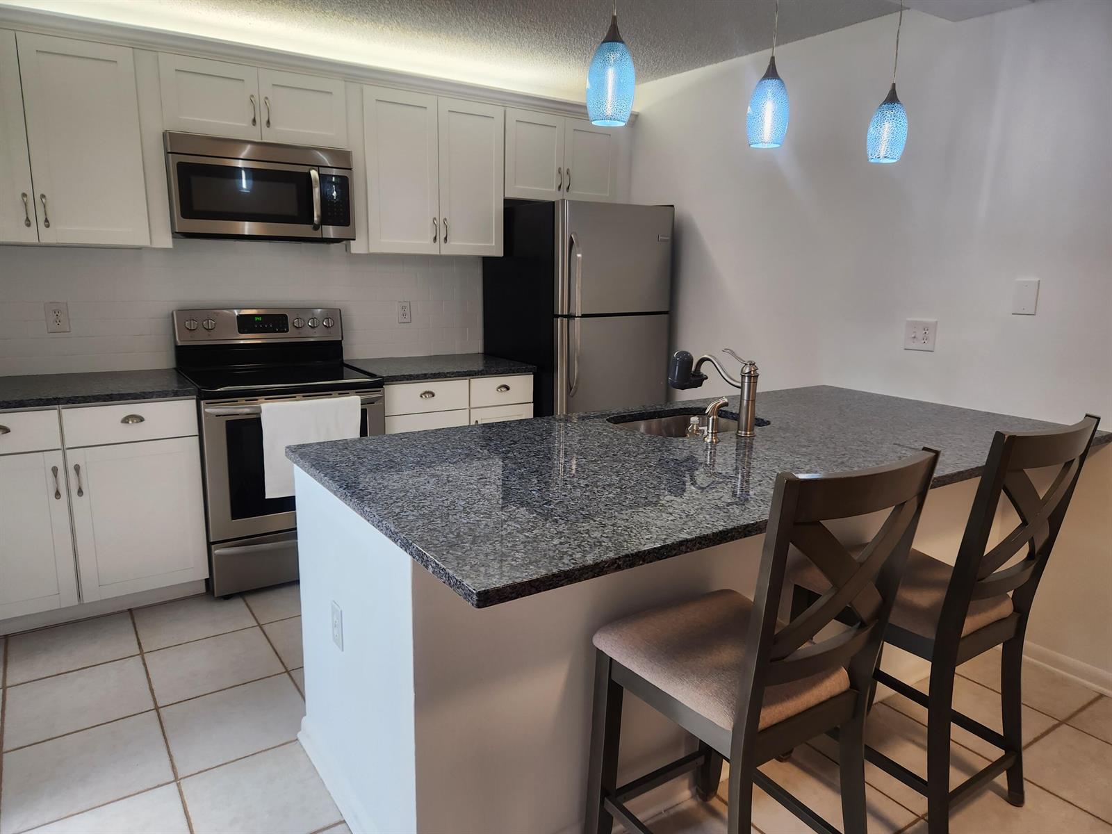 A kitchen features white cabinets, stainless steel appliances, granite countertops, and a breakfast bar island — 2813 28th Court, Jupiter FL 33477, JUPITER, FL