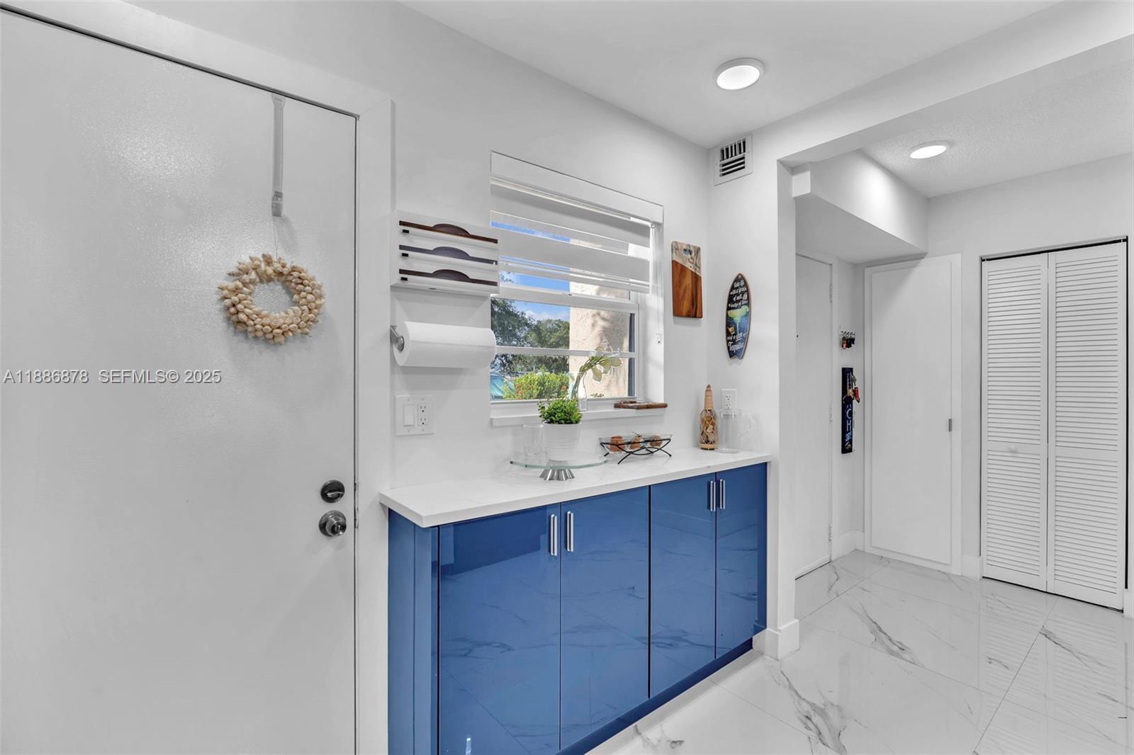 A room features blue cabinets, a white countertop, a window, and white tiled flooring — 205 SE 11th Terrace # 101, Dania Beach FL 33004, DANIA BEACH, FL