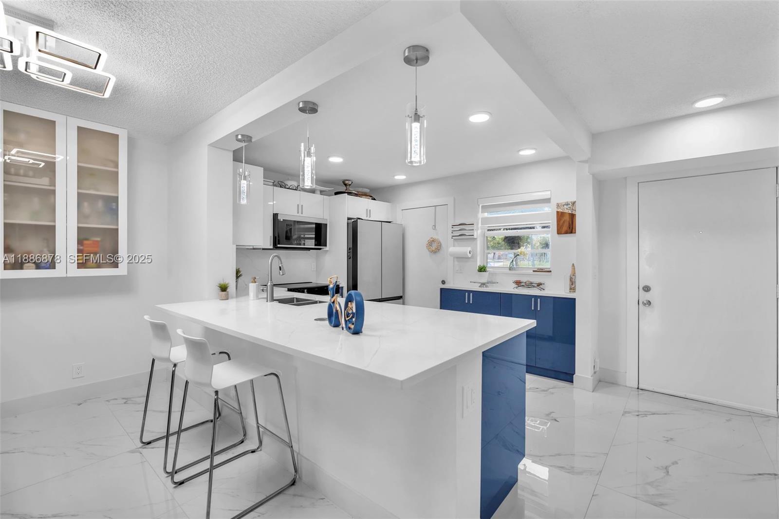 A modern kitchen features a white quartz island, blue lower cabinets, and white marble flooring — 205 SE 11th Terrace # 101, Dania Beach FL 33004, DANIA BEACH, FL