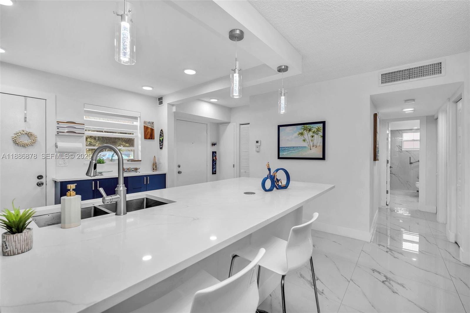 A modern kitchen features a white quartz island, blue cabinets, and white marble-look tile flooring — 205 SE 11th Terrace # 101, Dania Beach FL 33004, DANIA BEACH, FL