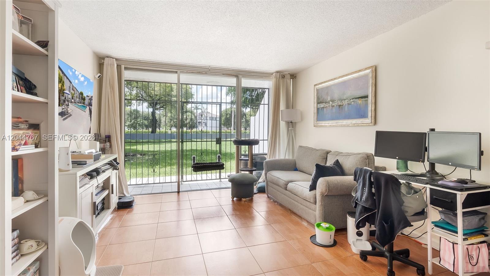 A living room features tile flooring, a sofa, a desk with monitors, and sliding glass doors — 110 Fontainebleau Blvd # 101, Miami FL 33172, MIAMI, FL