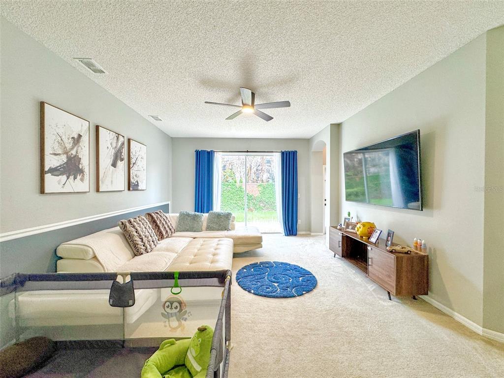A living room features a white sectional sofa, a wall-mounted television, and blue curtains — 1207 ROYAL SAINT GEORGE DRIVE, ORLANDO, FL