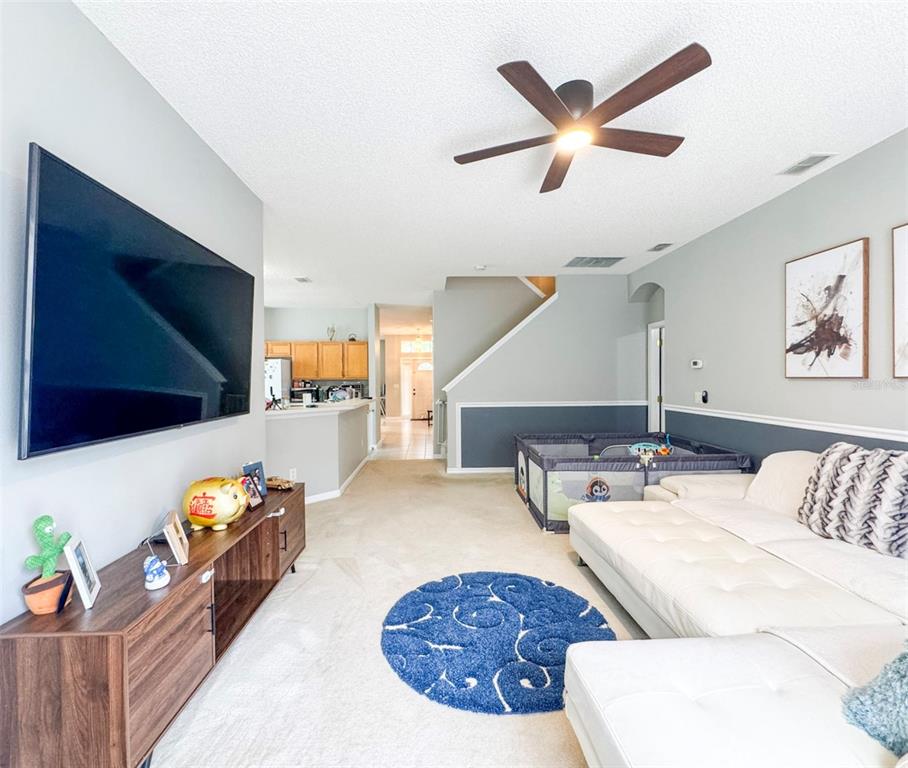 A living room features a large television, white sectional sofa, blue rug, and ceiling fan — 1207 ROYAL SAINT GEORGE DRIVE, ORLANDO, FL