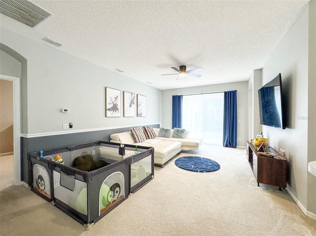 A living room features a large sectional sofa, a playpen, and a wall-mounted television — 1207 ROYAL SAINT GEORGE DRIVE, ORLANDO, FL