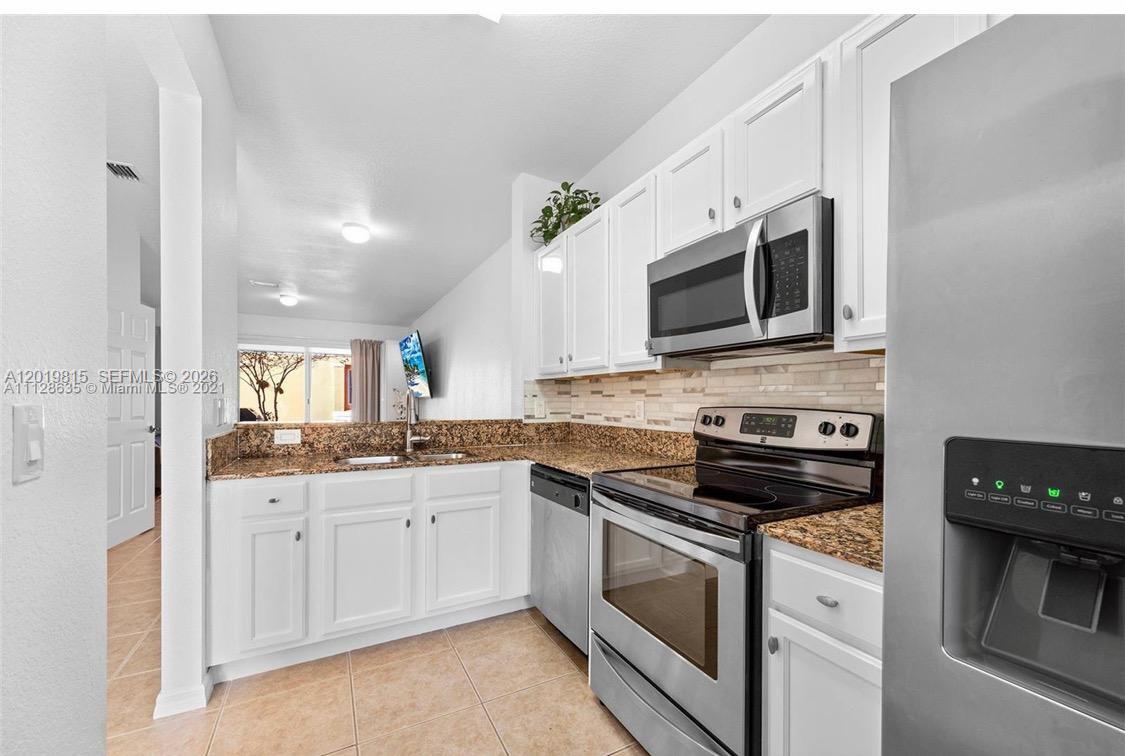 A kitchen features white cabinets, granite countertops, stainless steel appliances, and tile flooring — 1820 SW 89th Ter, Miramar FL 33025, MIRAMAR, FL