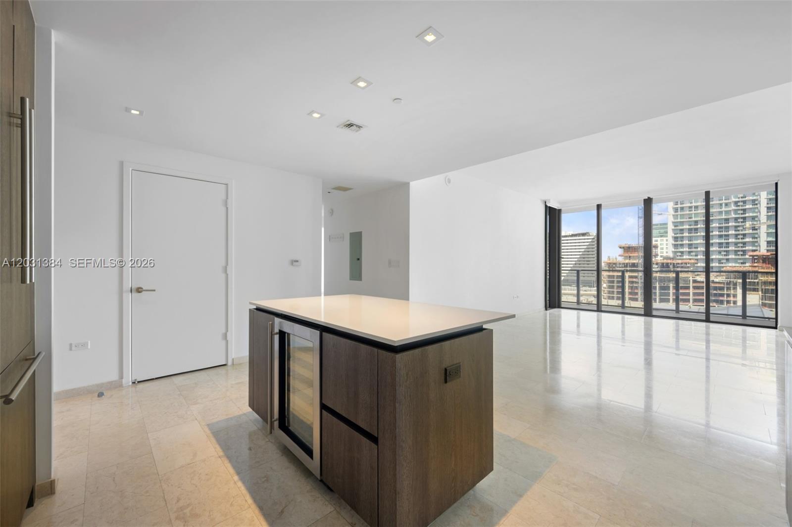 A modern kitchen island with a wine cooler sits in a bright, open-plan living space — 68 SE 6th St # 910, Miami FL 33131, MIAMI, FL