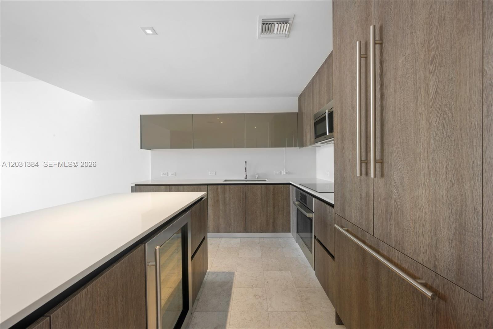 A modern kitchen features wood-grain cabinetry, a white island, and stainless steel appliances — 68 SE 6th St # 910, Miami FL 33131, MIAMI, FL
