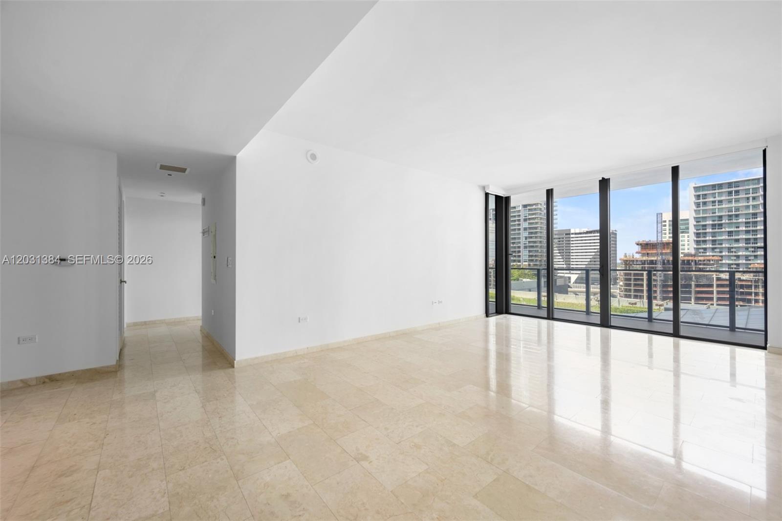An empty room with light-colored tile floors and floor-to-ceiling windows overlooking a city skyline — 68 SE 6th St # 910, Miami FL 33131, MIAMI, FL