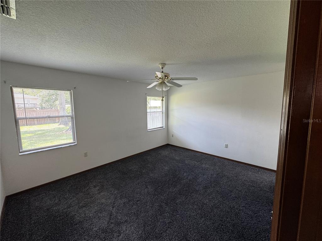 An empty bedroom features dark gray carpeting, white walls, two windows, and a ceiling fan — 4080 NE 28TH TERRACE, OCALA, FL