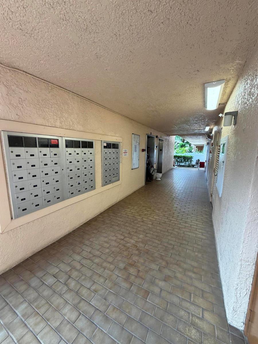 An outdoor hallway features a brick floor, beige walls, and a bank of metal mailboxes — 14575 Bonaire Boulevard # 206, Delray Beach FL 33446, DELRAY BEACH, FL