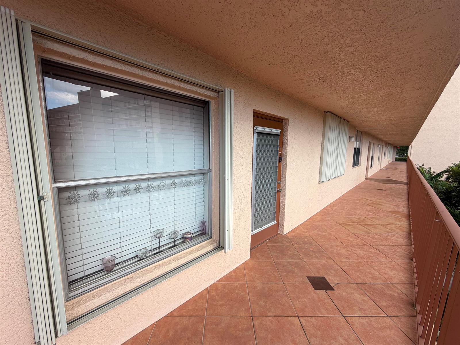 A tiled outdoor walkway runs along the exterior of a building with windows and doors — 14575 Bonaire Boulevard # 206, Delray Beach FL 33446, DELRAY BEACH, FL