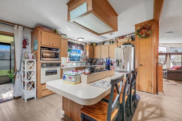 A kitchen features wood cabinets, a central island with bar seating, and stainless steel appliances — 357 WADE PARK COURT, DAVENPORT, FL