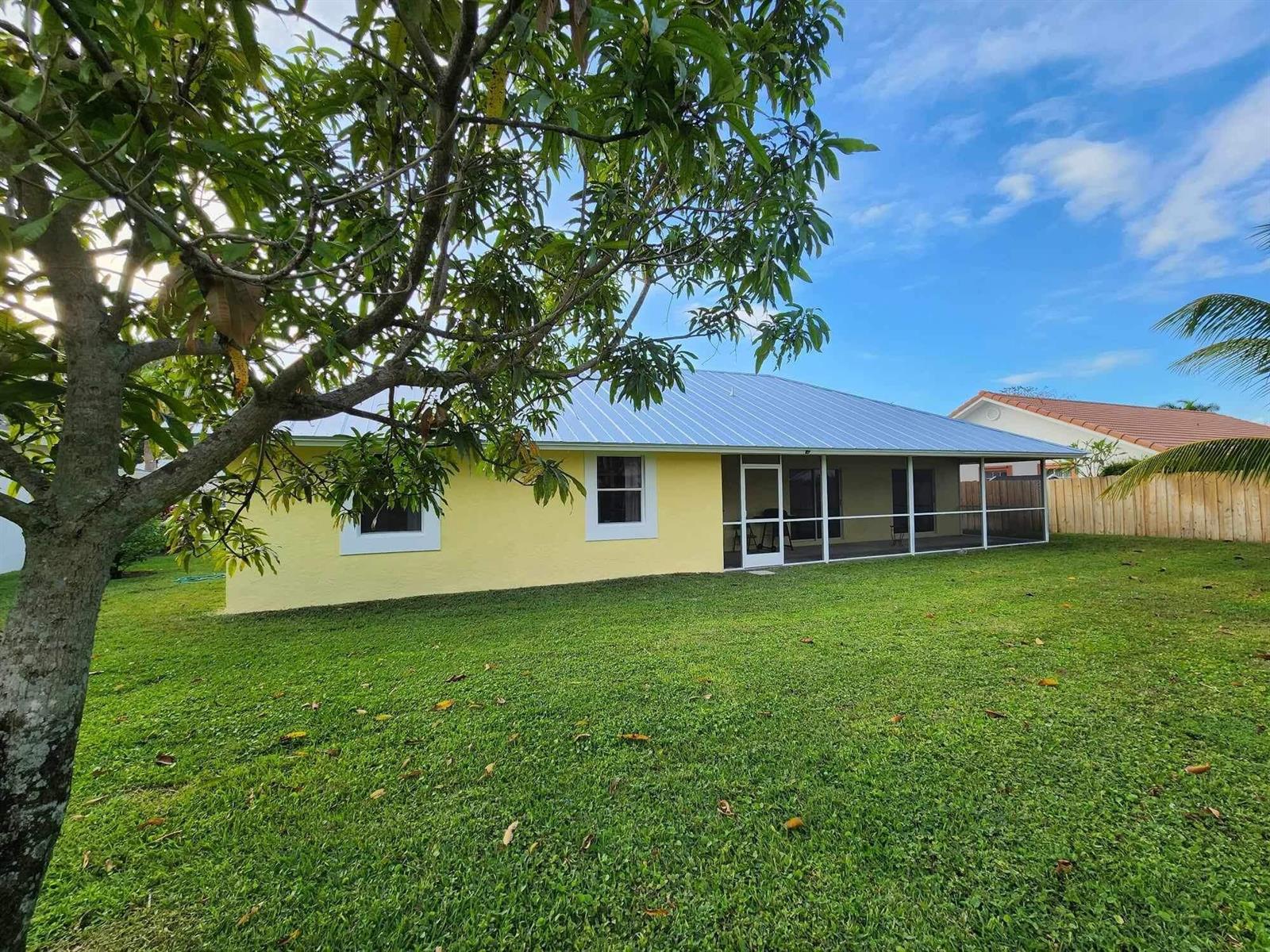 A yellow house with a metal roof and a screened-in back porch sits on grass — 1750 Primrose Lane, Wellington FL 33414, WELLINGTON, FL