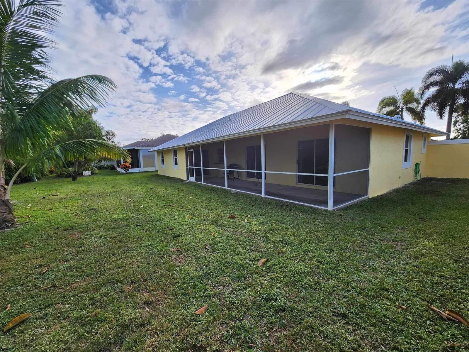 A yellow house with a metal roof and a screened-in back porch overlooks a lawn — 1750 Primrose Lane, Wellington FL 33414, WELLINGTON, FL