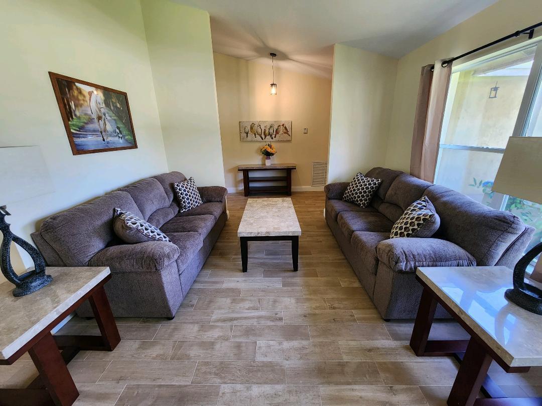 A living room features two gray sofas, a coffee table, and light wood-look tile flooring — 1750 Primrose Lane, Wellington FL 33414, WELLINGTON, FL