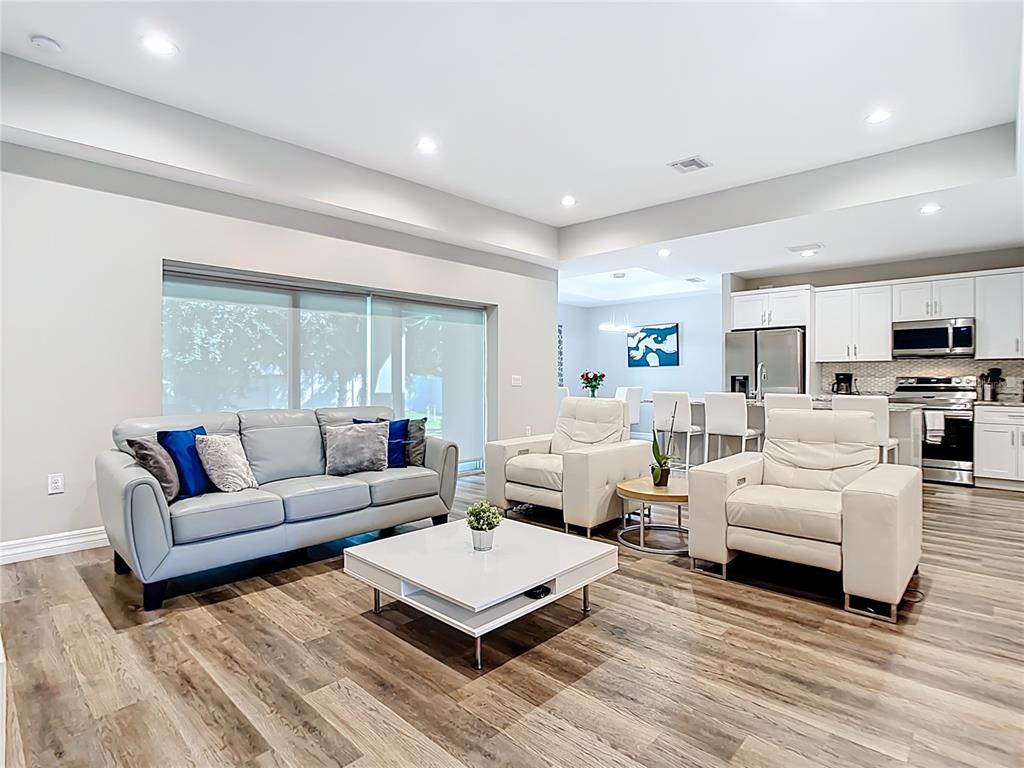 A living room with light gray flooring, a leather sofa, two armchairs, and an open kitchen — 5153 PINSON DRIVE, NORTH PORT, FL