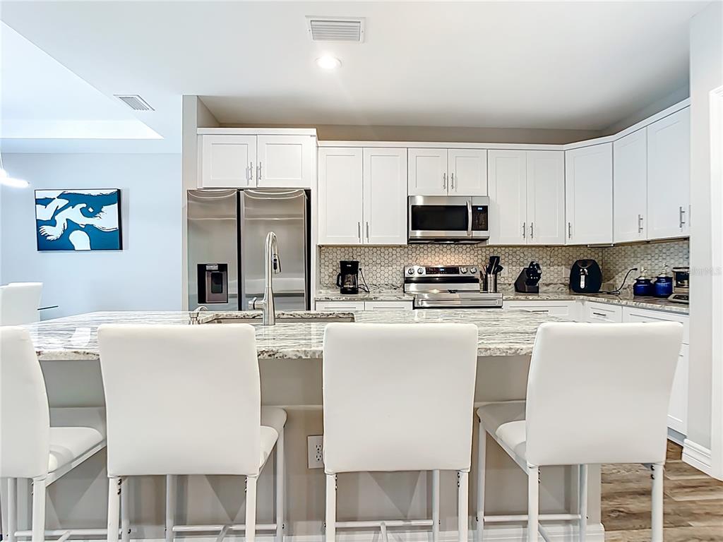 A modern kitchen features white cabinets, granite countertops, a large island, and stainless steel appliances — 5153 PINSON DRIVE, NORTH PORT, FL